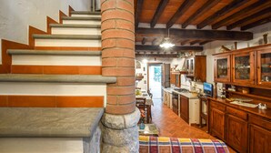 A staircase with a brick pillar, leading to a kitchen with wooden cabinets and a dining area.