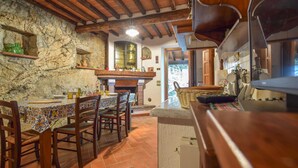 A rustic kitchen with stone walls, wooden beams, and a tiled floor.
