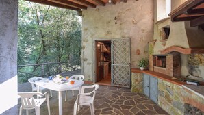 An outdoor patio with a stone floor, white plastic chairs, a table with a white tablecloth, and a brick fireplace.