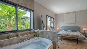 A modern bathroom with a bathtub, a window with a view of greenery, and a bed with a view of the bathroom. - Stunning home in Solliès-Toucas (Solliès-Toucas)