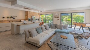A modern kitchen with a central island, a dining area with a table and chairs, a large sofa, and a view of greenery through large windows. - Stunning home in Solliès-Toucas (Solliès-Toucas)