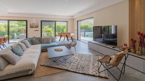 A spacious living room with a sectional sofa, a coffee table, and a TV. There is a dining area with a table and chairs, and a pool visible through large windows. - Stunning home in Solliès-Toucas (Solliès-Toucas)