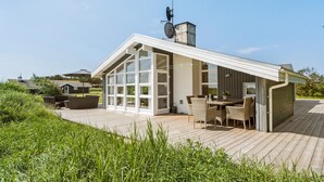A modern house with a large glass door, a wooden deck, and a dining area with wicker furniture. - Stunning home in Ringkøbing with sauna (Ringkøbing)