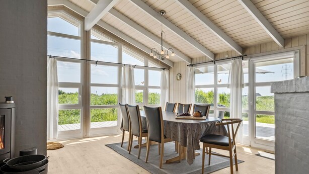 A dining area with a large table, chairs, and a view of greenery through large windows. - Stunning home in Ringkøbing with sauna (Ringkøbing)