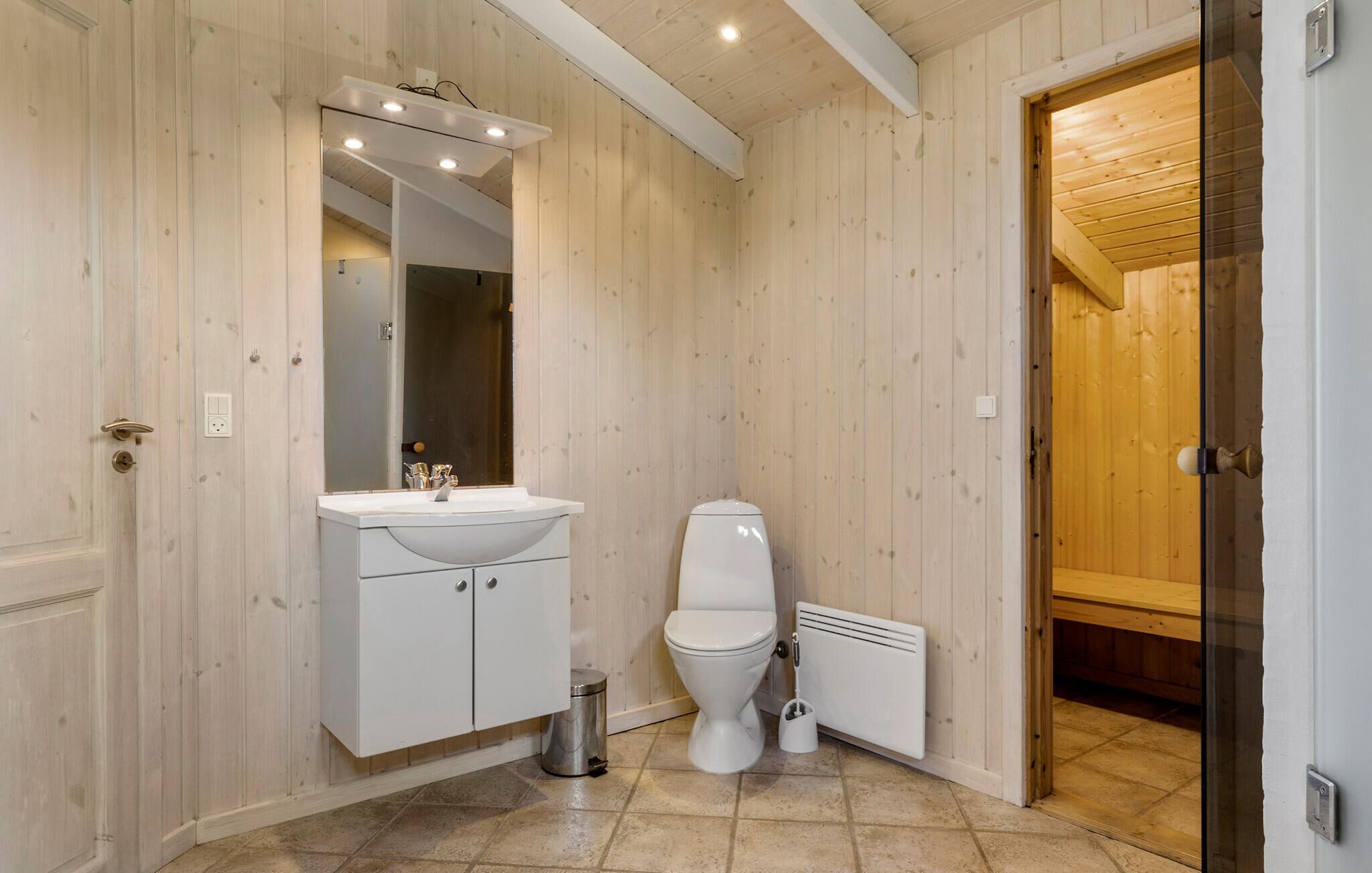 Une salle de bain avec des murs en bois, un lavabo blanc, des toilettes et un espace douche.