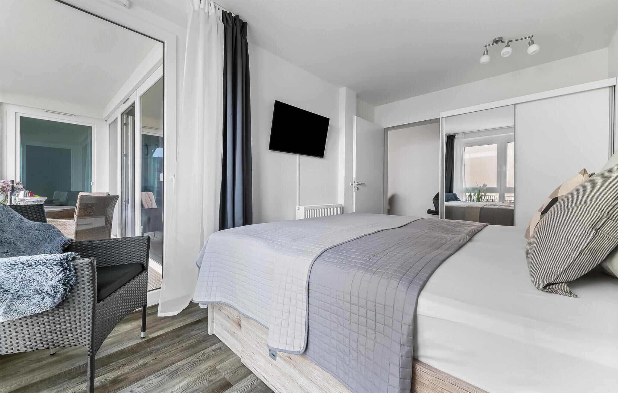 Ein modernes Hotelzimmer mit einem großen Bett, einem flachbildfernseher an der Wand und einem Balkon mit Sitzgelegenheit.