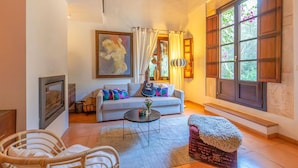 A living room with a sofa, a guitar, a painting, and a large window with curtains. - Amazing home in Capdepera (Capdepera)