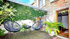 A wooden deck with two wicker chairs and a small table, surrounded by greenery and a stone wall. - 3 bedroom pet friendly home in Castelreng (Castelreng)