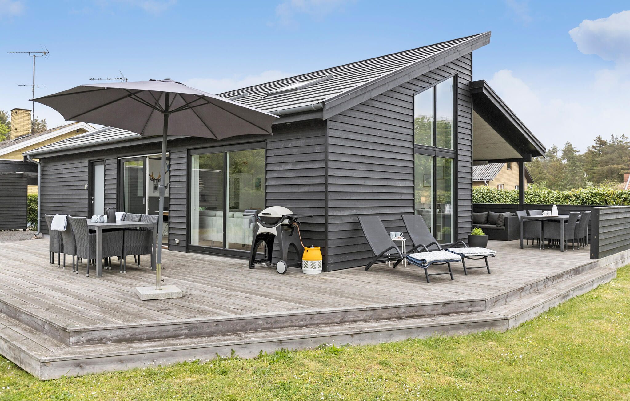 A modern outdoor deck with a dining area, a covered seating area, and a large umbrella providing shade.