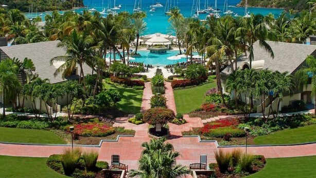 Ein Resort mit einem zentralen Pool, umgeben von Palmen und Blick auf das Meer mit Booten.