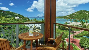 Ein Holztisch und -stühle auf einem Balkon mit Blick auf eine tropische Landschaft und das Meer.