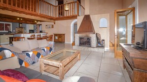 A spacious living room with a high ceiling, a fireplace, a dining area, and a television.