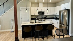 Una cocina moderna con armarios blancos, un refrigerador de acero inoxidable, una isla central con taburetes altos e iluminación colgante.