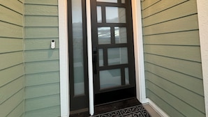 Puerta principal con panel de vidrio, felpudo y buzón en la pared.