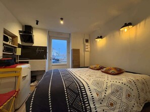 Une chambre à coucher avec un lit, un bureau, une chaise, une fenêtre et une vue sur l’extérieur.