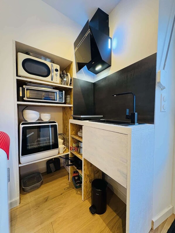 Une cuisine compacte équipée d’un four à micro-ondes, d’un four traditionnel et d’une cuisinière, ainsi que d’étagères en bois et d’une poubelle.