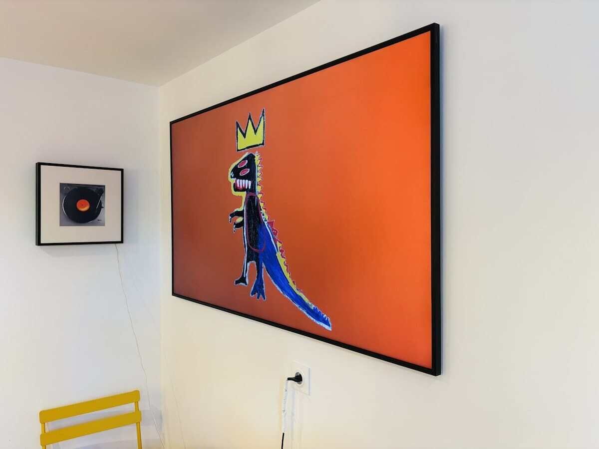 Ein Zimmer mit einem großen gerahmten Kunstwerk eines Dinosauriers mit Krone, einer gerahmten Schallplatte und einem gelben Stuhl.