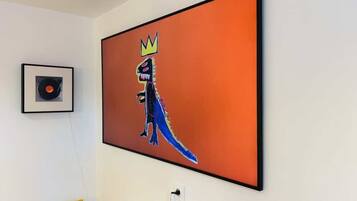A room with a large framed artwork of a dinosaur wearing a crown, a framed vinyl record, and a yellow chair.