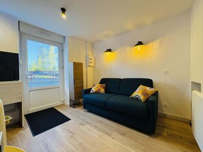 Ein modernes Wohnzimmer mit einer Couch, zwei gemusterten Kissen, einem Fernseher und einer Glasschiebetür, die auf einen Balkon führt.