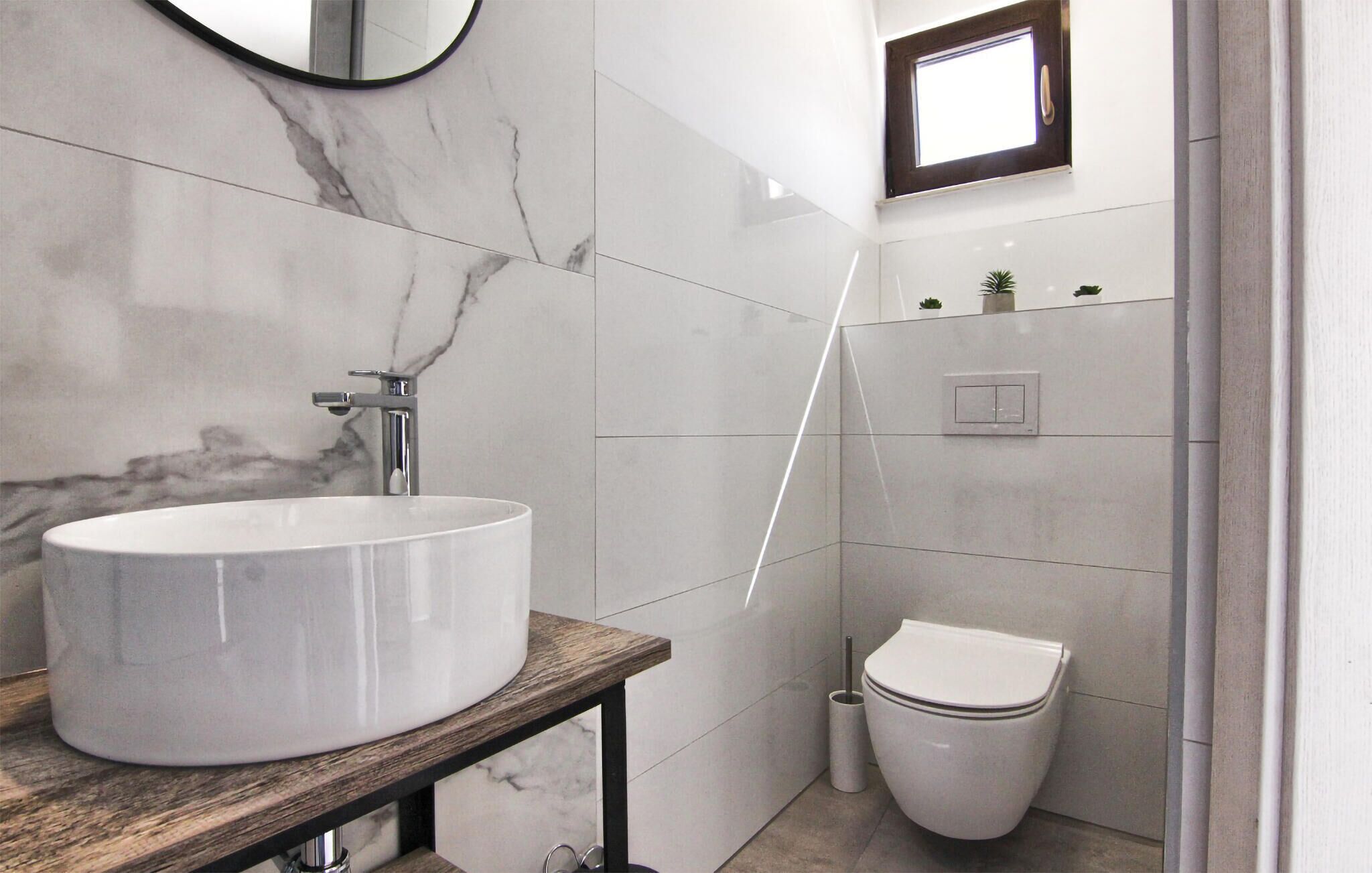 A bathroom with a large white sink, a wooden countertop, a toilet, and a small window.