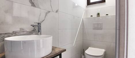 A bathroom with a large white sink, a wooden countertop, a toilet, and a small window.