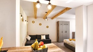 Una sala moderna con techo de madera, un sofá negro, una mesa de comedor con fruta y una cama con una manta amarilla.