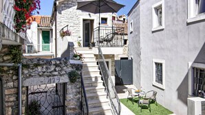 Un patio con una escalera de piedra que lleva a un edificio con balcón. Hay un pequeño espacio al aire libre con una mesa y sillas.