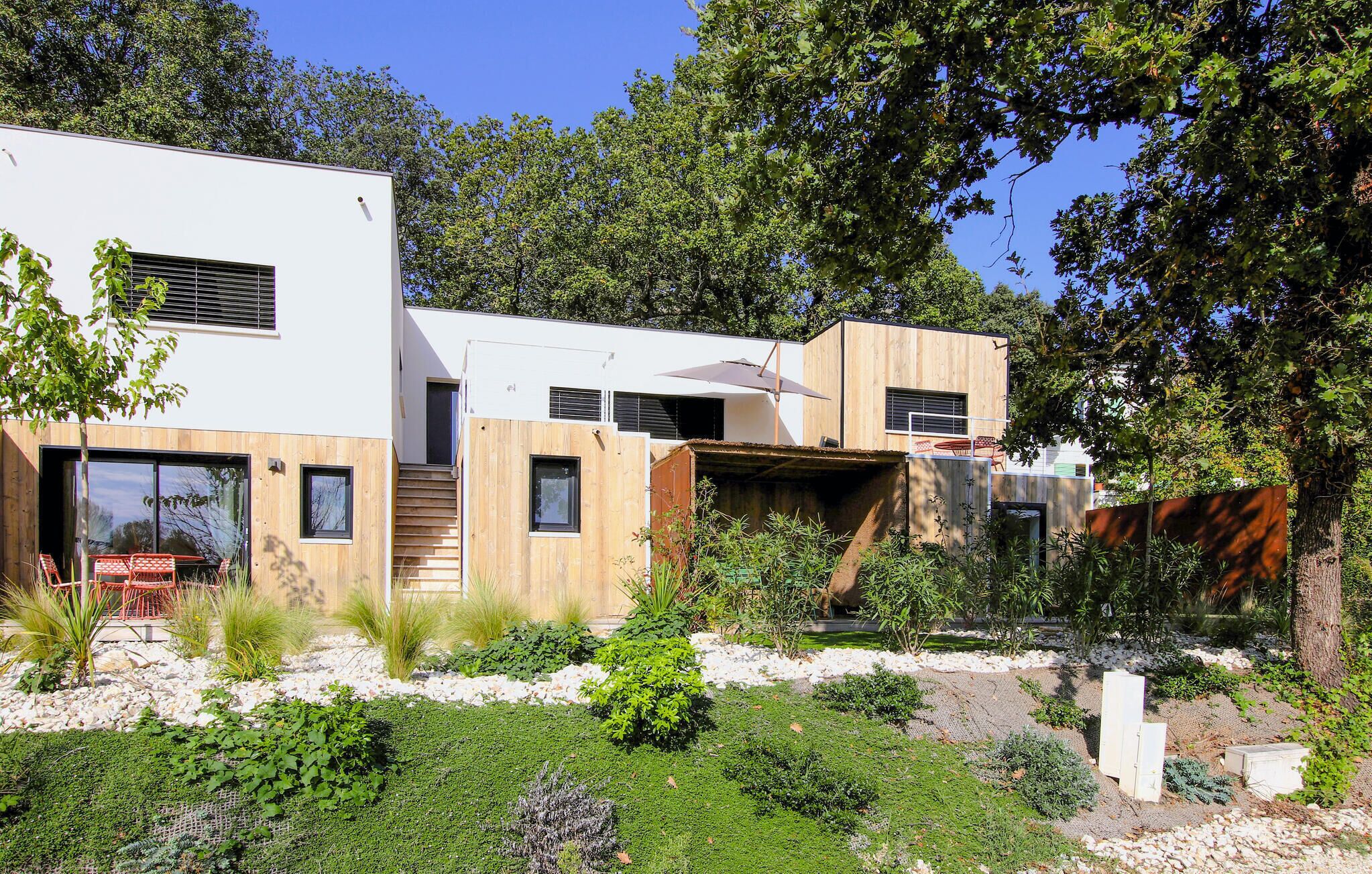 Ein modernes, zweistöckiges Haus mit minimalistischem Design, große Fenster und eine Holzterrasse.