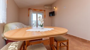 Una habitación pequeña y acogedora con una mesa redonda de madera, dos sillas, un televisor montado en la pared y una ventana con cortinas.