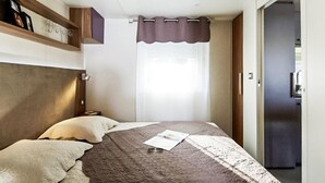Ein Schlafzimmer mit Bett, Kopfstütze, einem Fenster mit Vorhang und einer Tür zu einem weiteren Raum.