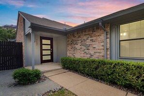 A two-story house with a brick exterior, a dark front door, and a small front yard with a hedge and a pathway. - The Retreat at The Colony (The Colony)