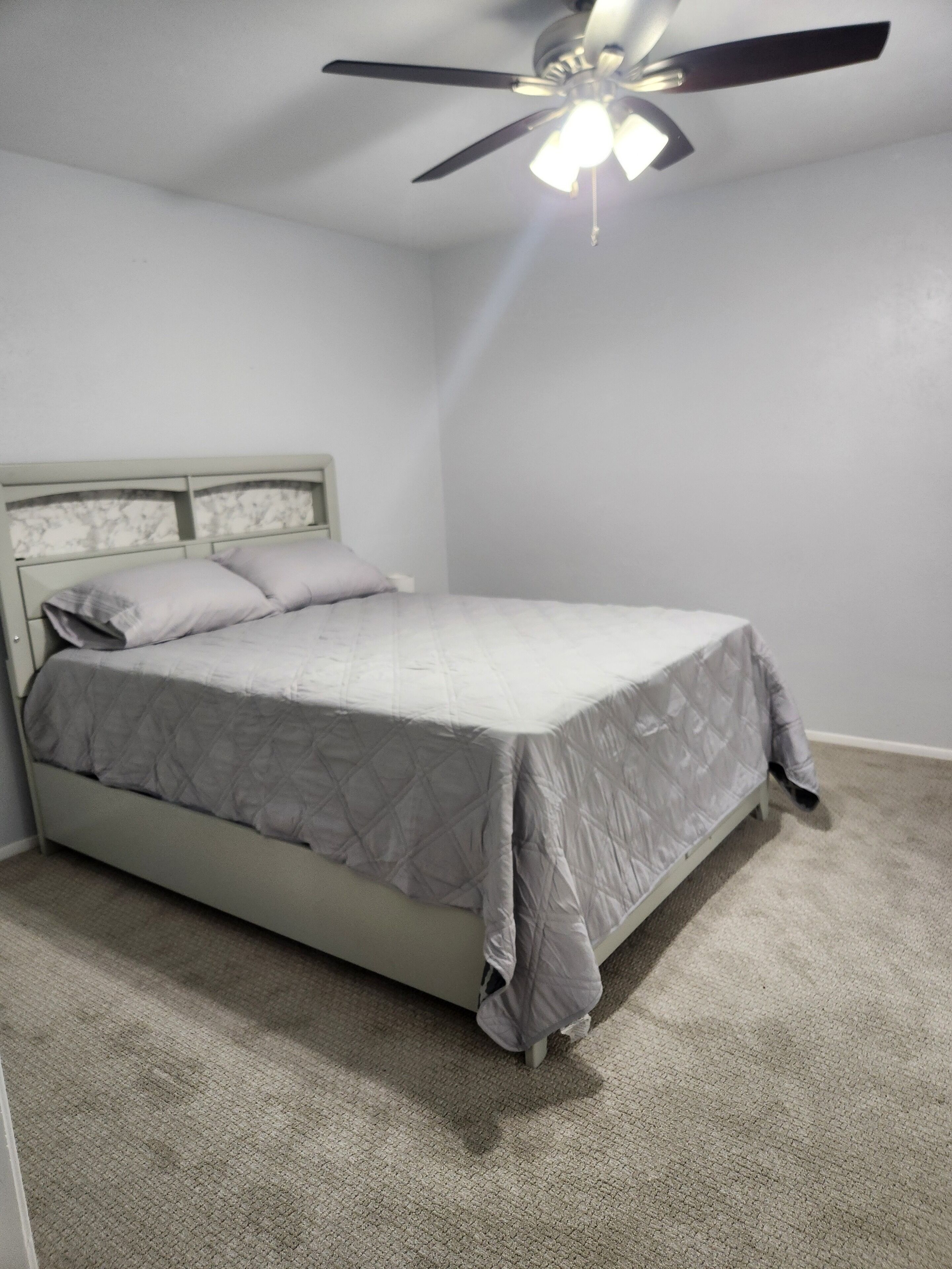 Un dormitorio con cama, ventilador de techo y piso alfombrado.