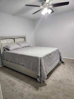 A bedroom with a bed, a ceiling fan, and a carpeted floor.