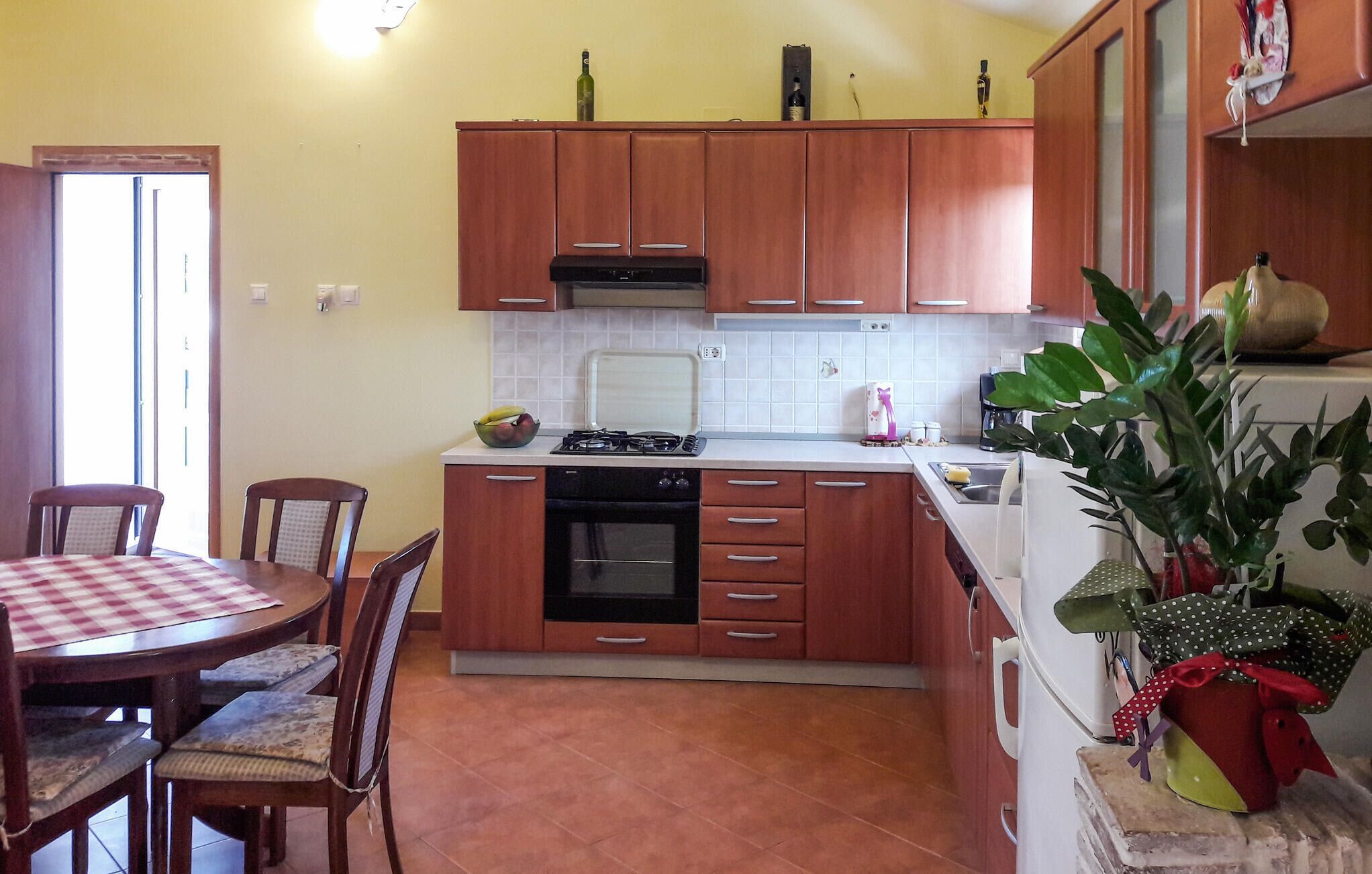 Una cocina compacta con armarios de madera, estufa, horno y una zona de comedor con mantel a cuadros.