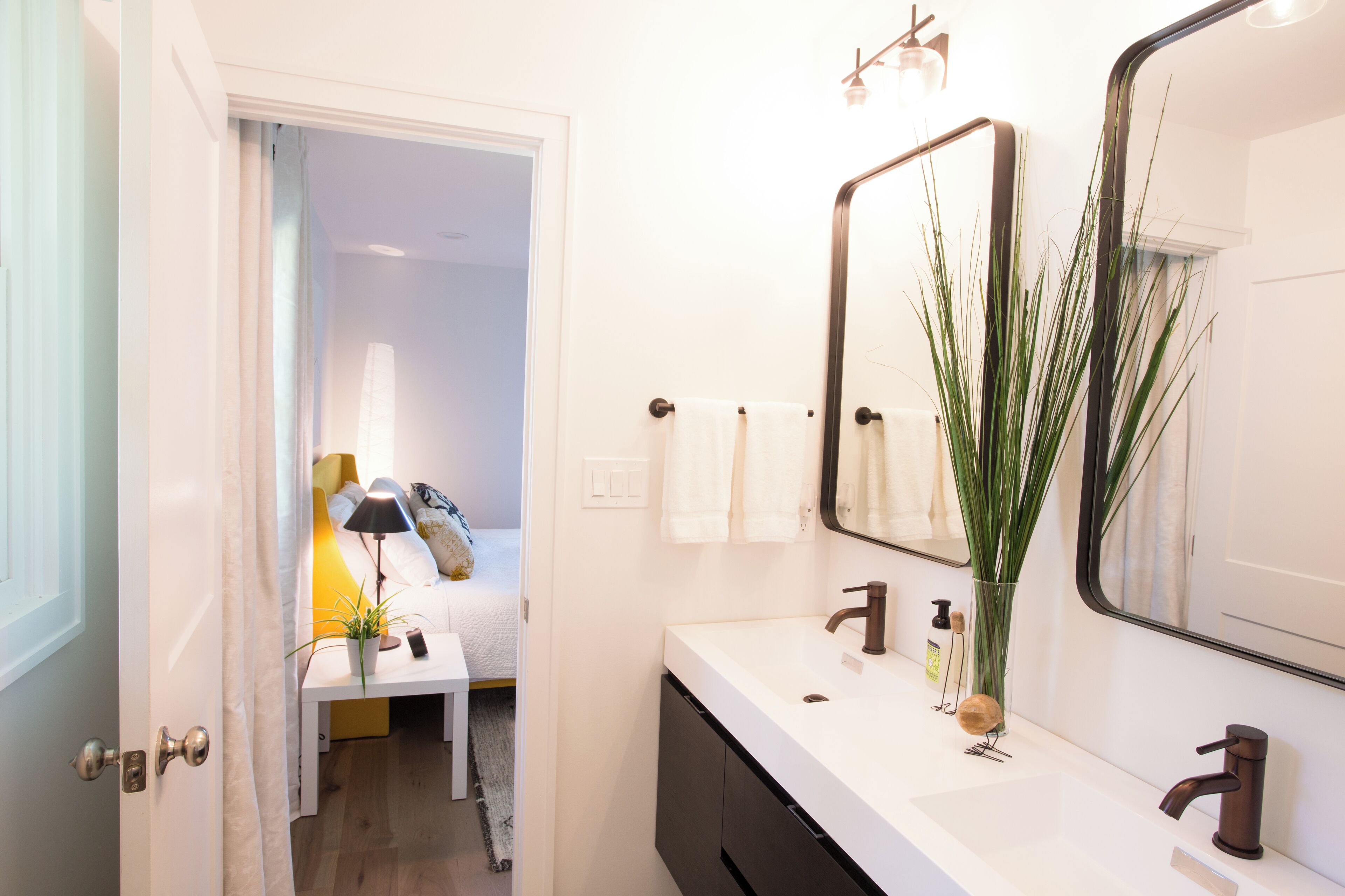 Een badkamer met een wit wastafelmeubel, een spiegel en een plant.