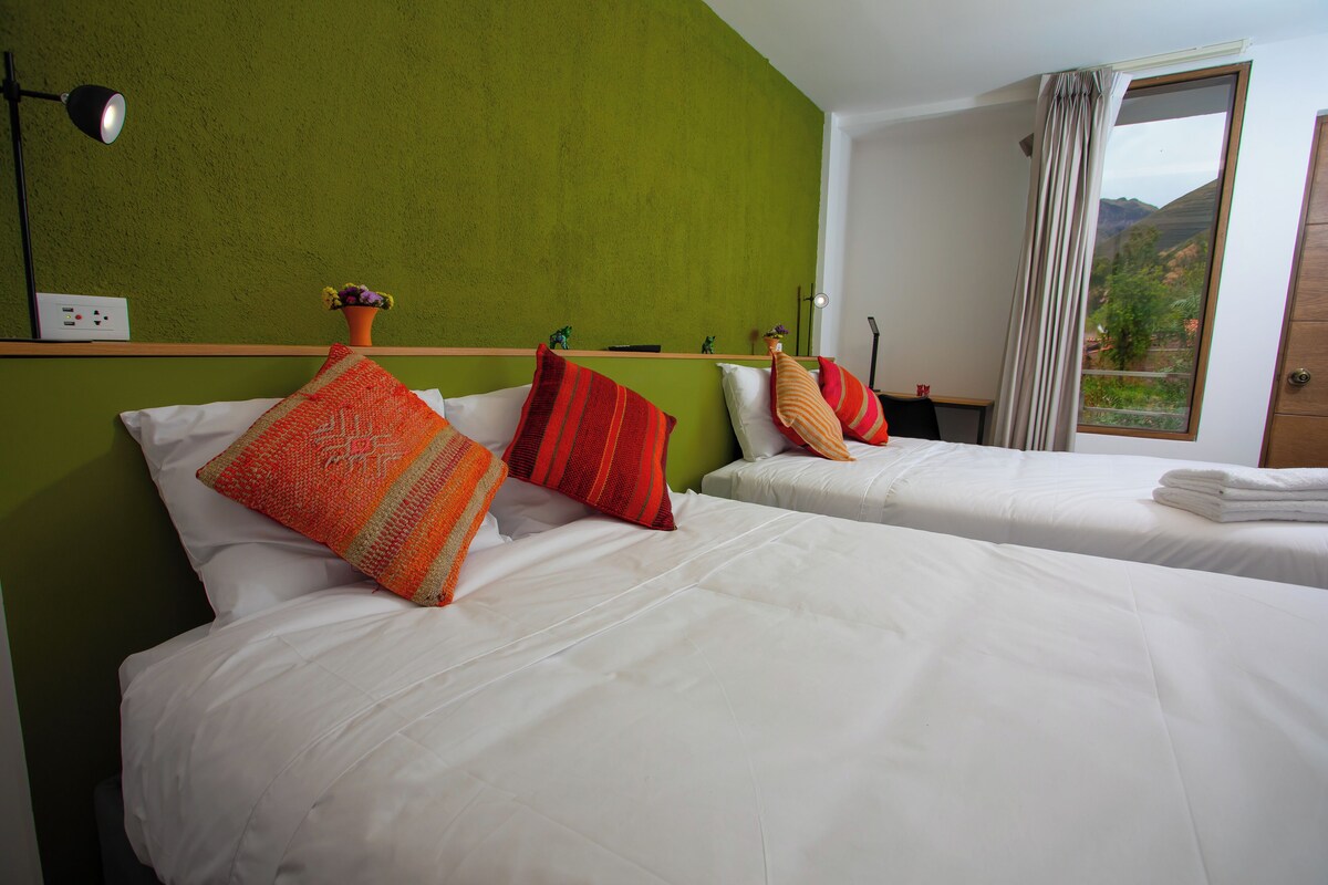 Una habitación de hotel con dos camas, paredes verdes, ropa de cama blanca y una ventana con vistas.