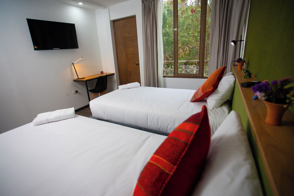 Habitación de hotel con dos camas, un escritorio, un televisor y una ventana con cortinas.