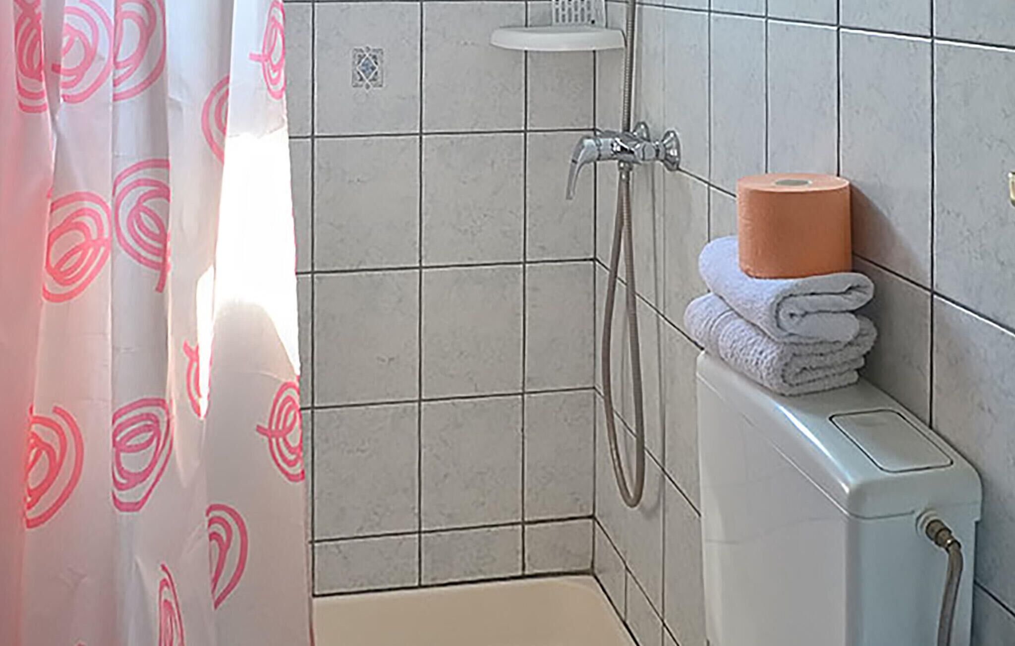 Et badeværelse med bruser, toilet og et stabel håndklæder på væggen.