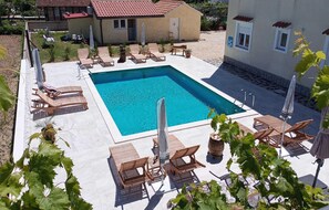 Une piscine carrée entourée de chaises longues en bois et de parasols, avec un petit bâtiment en arrière-plan.