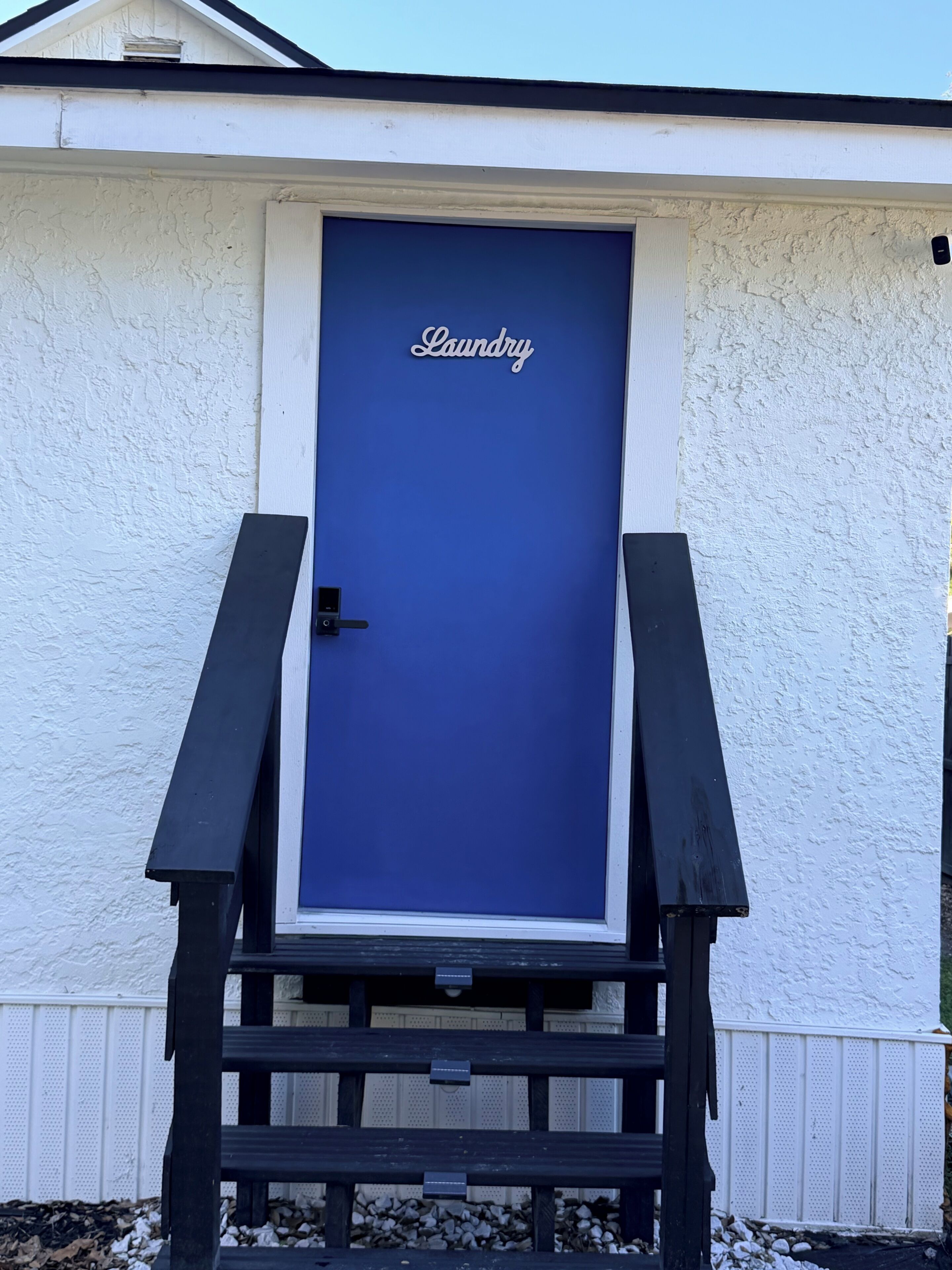 Una puerta azul con la palabra 'Laundry' escrita, ubicada en un edificio blanco de diseño sencillo.