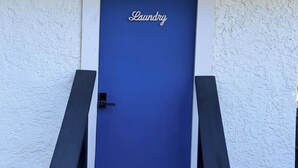 Una puerta azul con la palabra 'Laundry' escrita, ubicada en un edificio blanco de diseño sencillo.