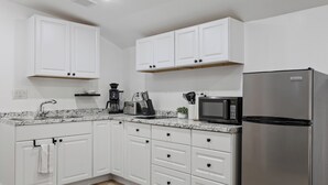 Una cocina moderna con armarios blancos, un refrigerador de acero inoxidable, un microondas y una cafetera.