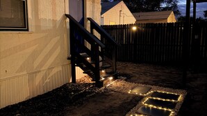Un sendero con bordes iluminados, una escalera de madera y un edificio con una puerta que dice 'Landings'.