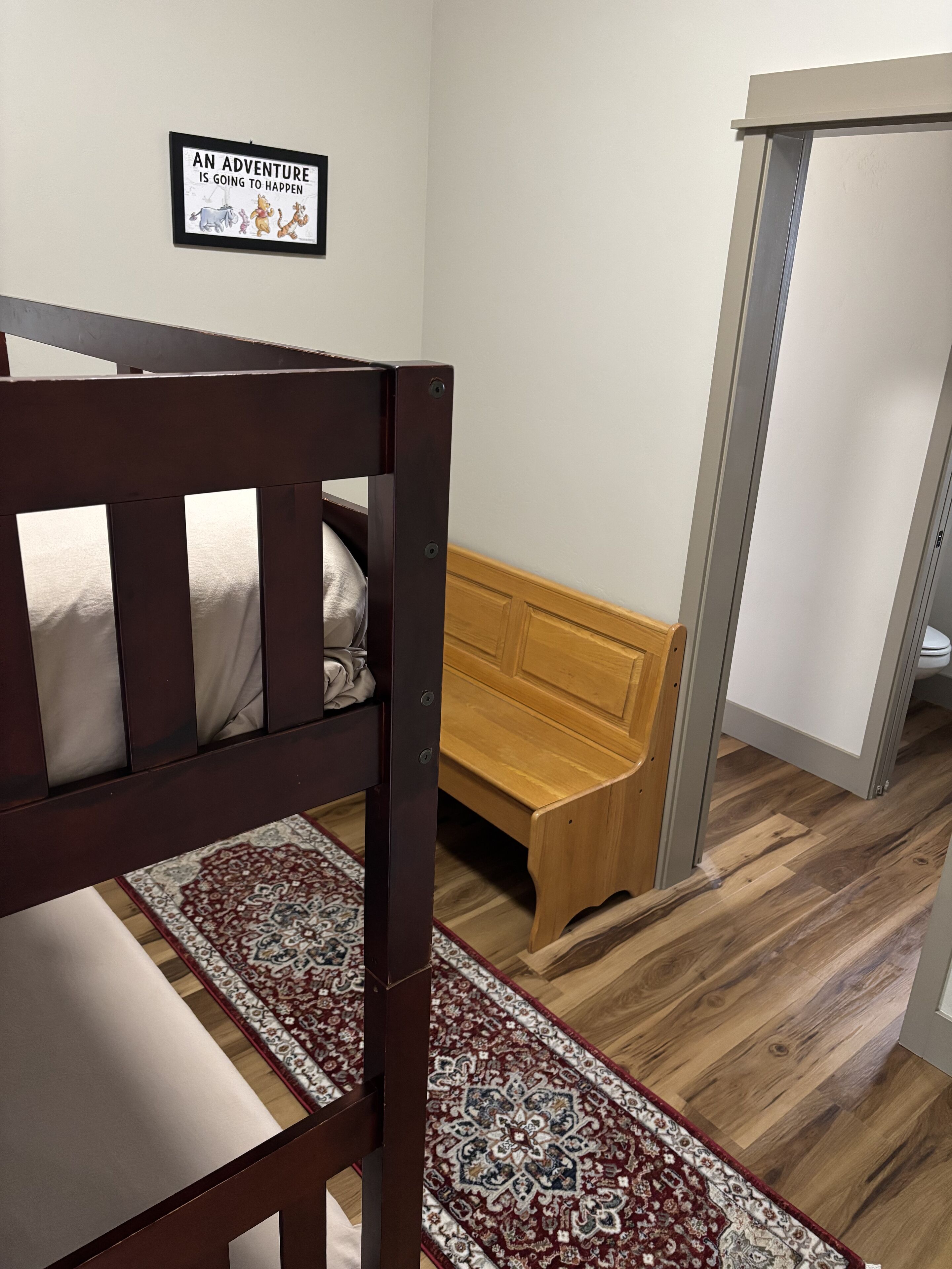 Un dormitorio con una cama litera, un banco de madera, un tapete estampado y una cita enmarcada en la pared.