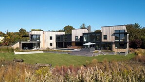 Une maison moderne à deux étages, dotée d’un grand jardin à l’avant, d’une piscine et d’un patio aménagé avec du mobilier d’extérieur.
