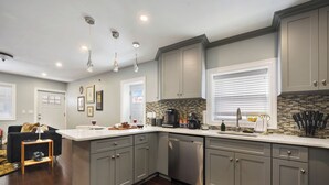 Una cocina moderna con armarios grises, encimera blanca y electrodomésticos de acero inoxidable. Hay una pequeña isla con un lavabo y una cafetera.