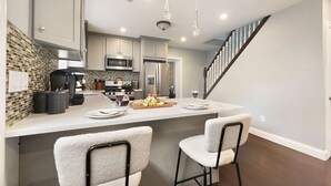Una cocina moderna con una isla central, electrodomésticos de acero inoxidable y una escalera que sube a otro nivel.