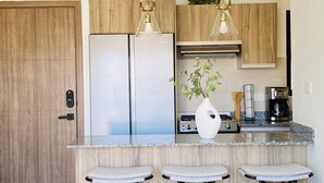 A modern kitchen with a stainless steel refrigerator, a gas stove, and a coffee maker. There are three bar stools and a white vase with green plants on the counter. - Stylish and Modern Apartment in Punta Cana (Punta Cana)
