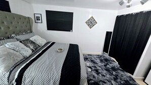 A bedroom with a bed, a window, a wall decoration, and a ceiling fan. - COZY 1Br Basement Suite Perfect for Couple!Free Sparkling Wine! Private Parking. (Burnaby)
