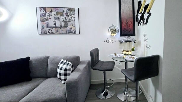 A modern living room with a grey sofa, a small round table with a bottle and glasses, and a framed picture on the wall. - COZY 1Br Basement Suite Perfect for Couple!Free Sparkling Wine! Private Parking. (Burnaby)